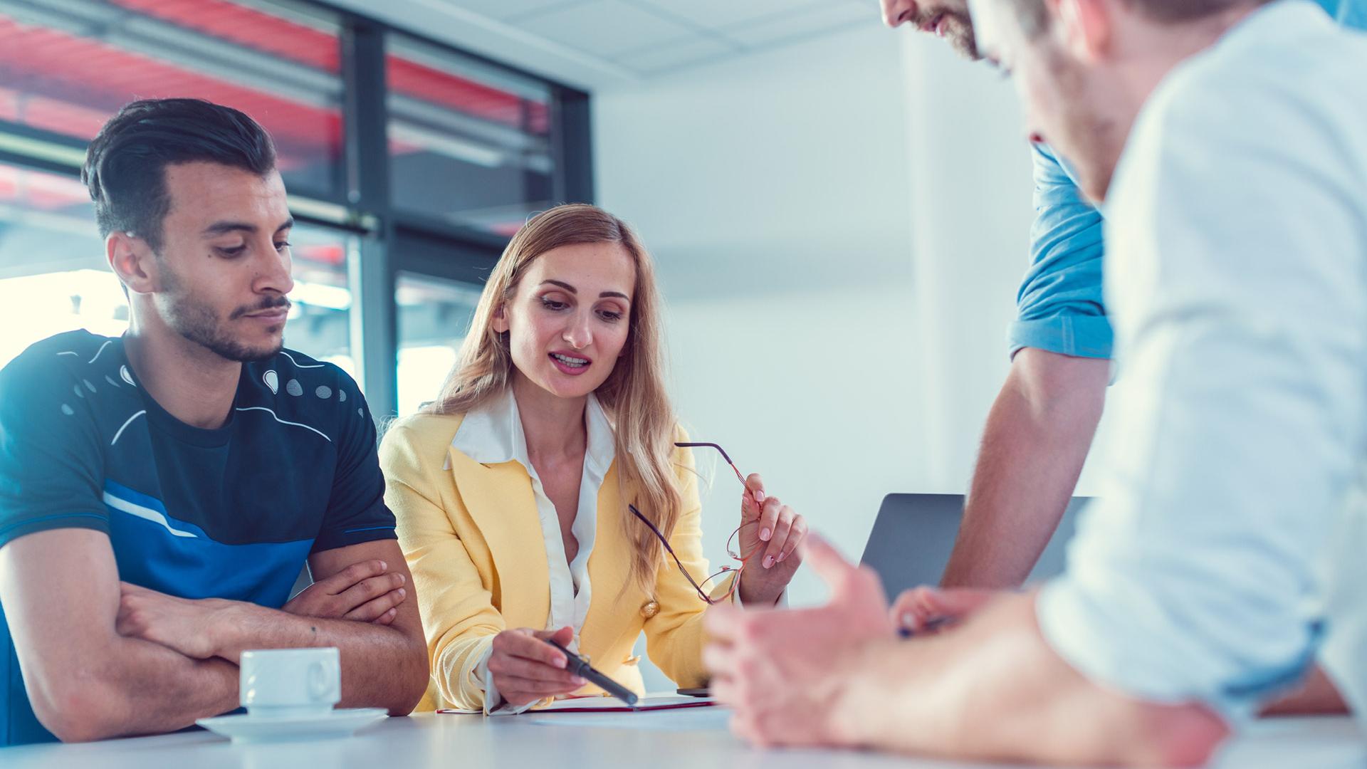Group of people discussing around a table in an office setting.