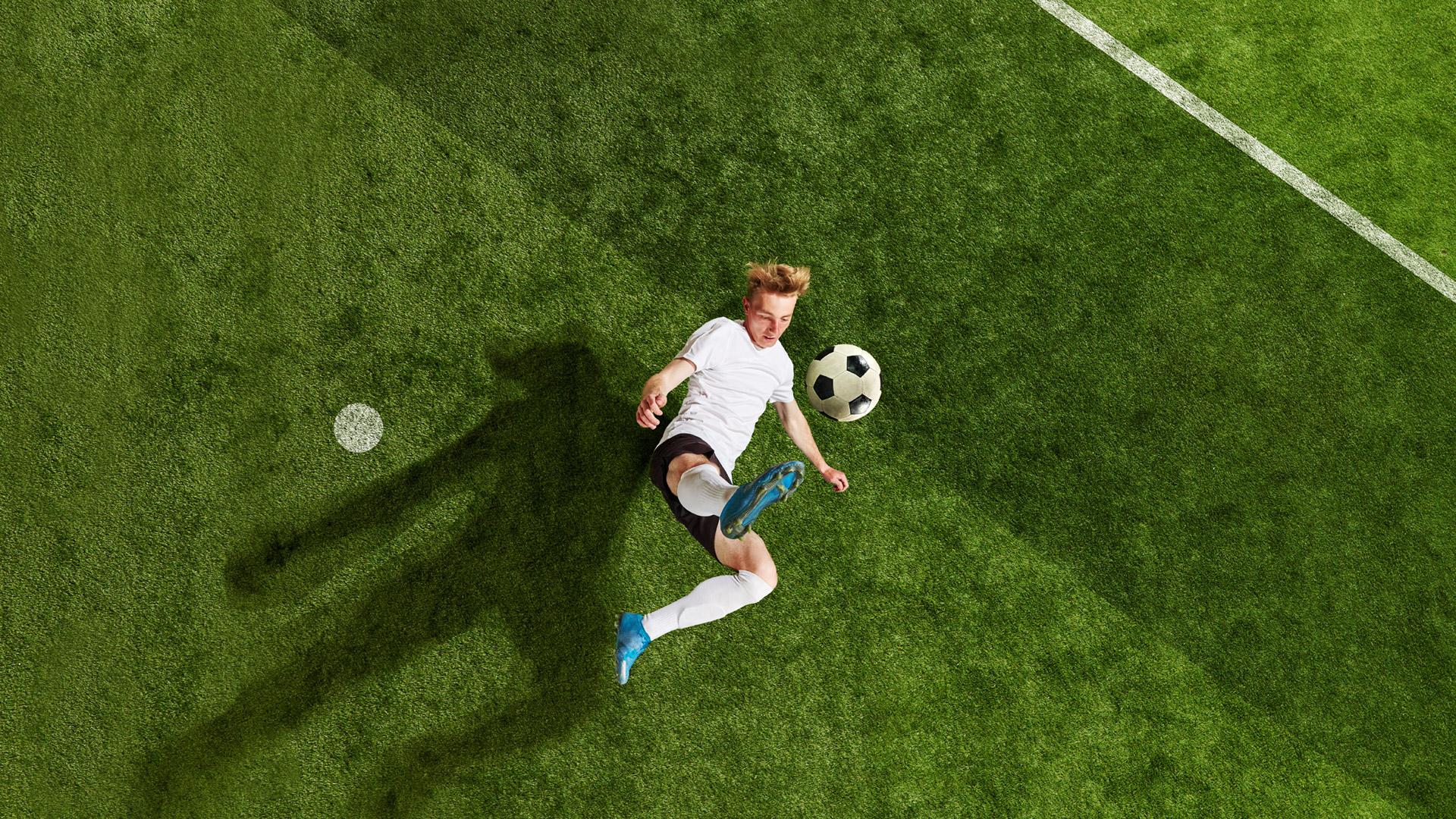 Soccer player performs a bicycle kick on a green soccer field.