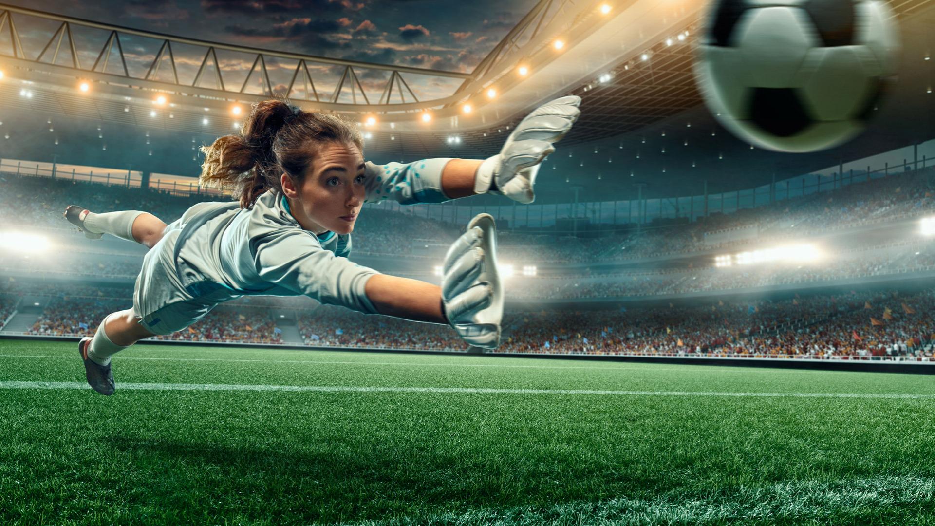 Goalkeeper diving to save a goal in a crowded stadium.