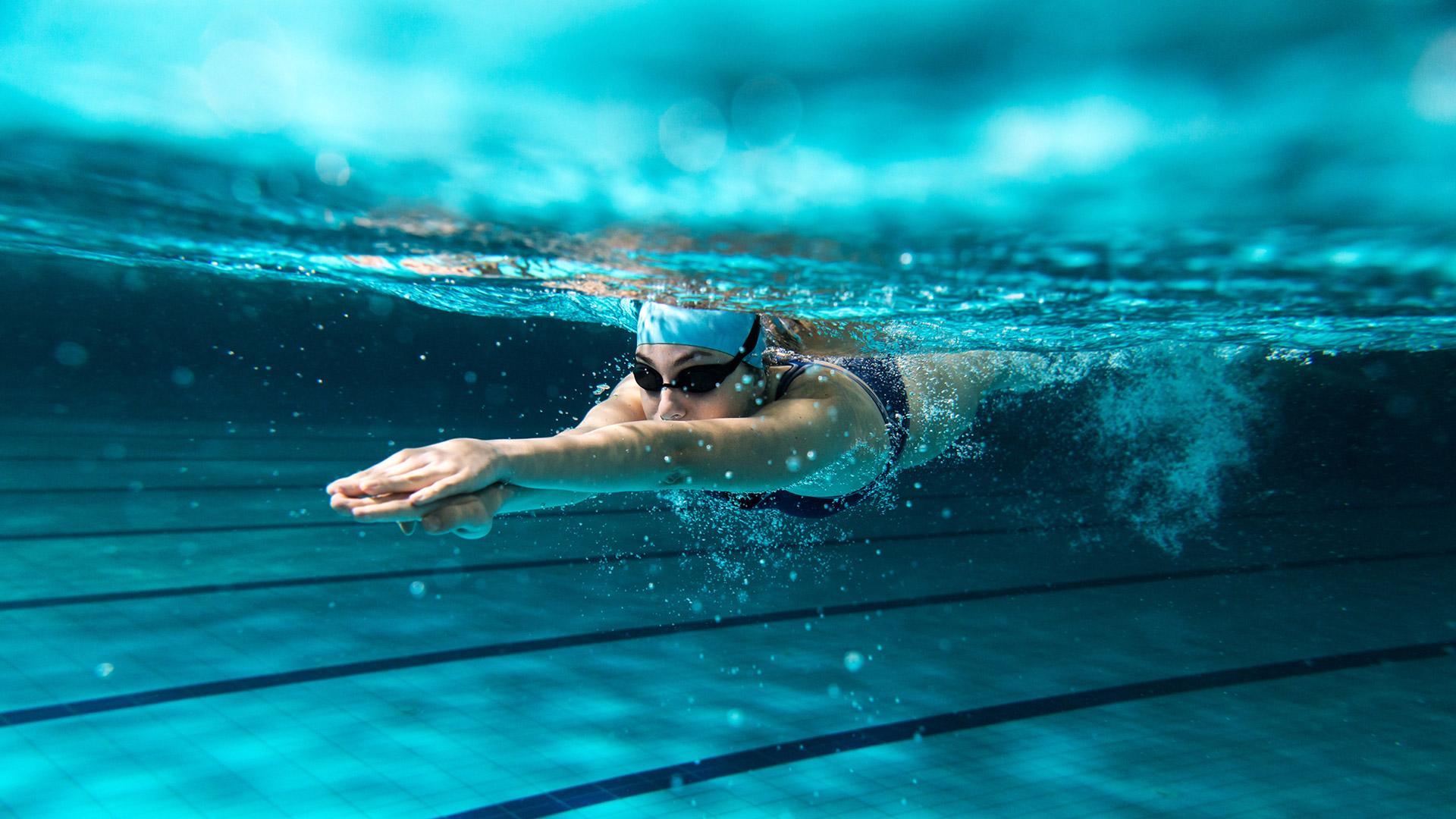 A swimmer underwater in a pool, wearing goggles and a swim cap.