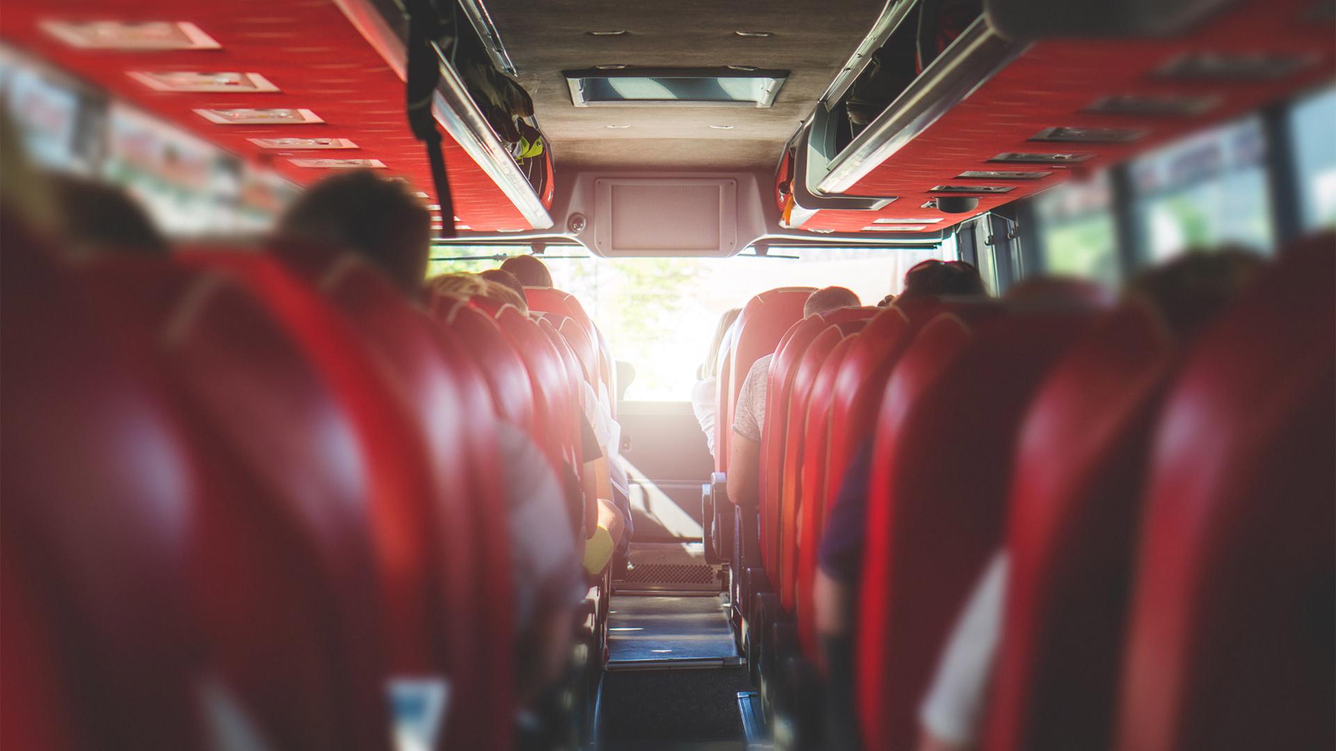 Interior of a bus with red seats and seated passengers.