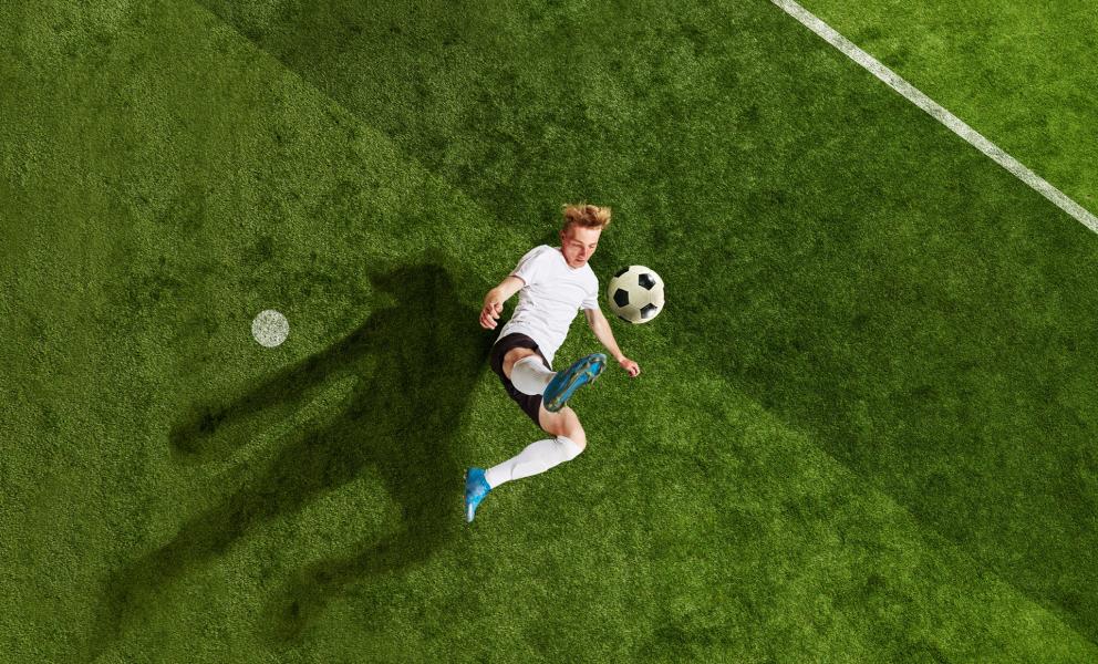 Soccer player performs a bicycle kick on a green soccer field.